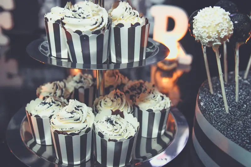 Tiered stand of cupcakes in black and white striped cases, beside cake pops and an illuminated letter