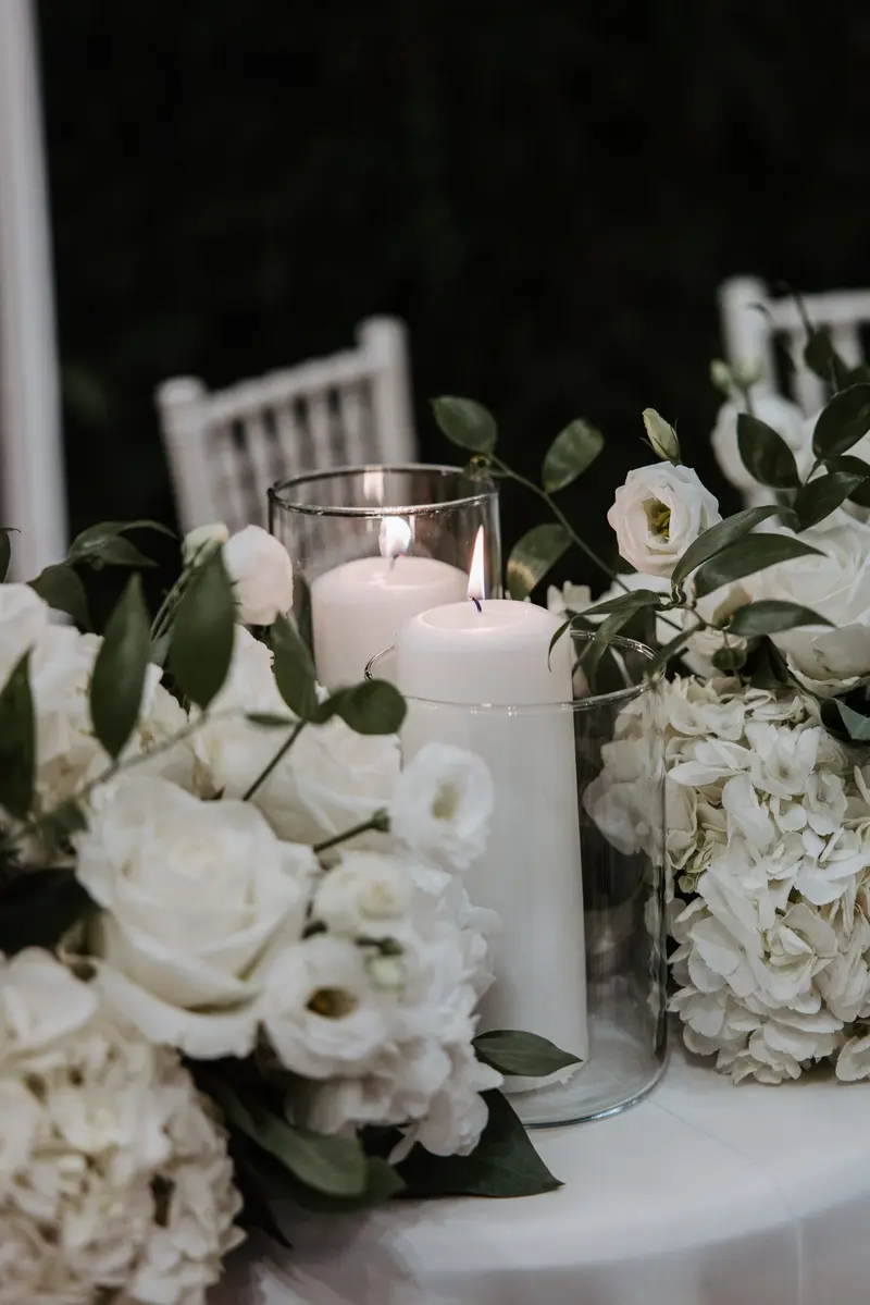 Pillar candles burning low among white roses and eucalyptus after dark