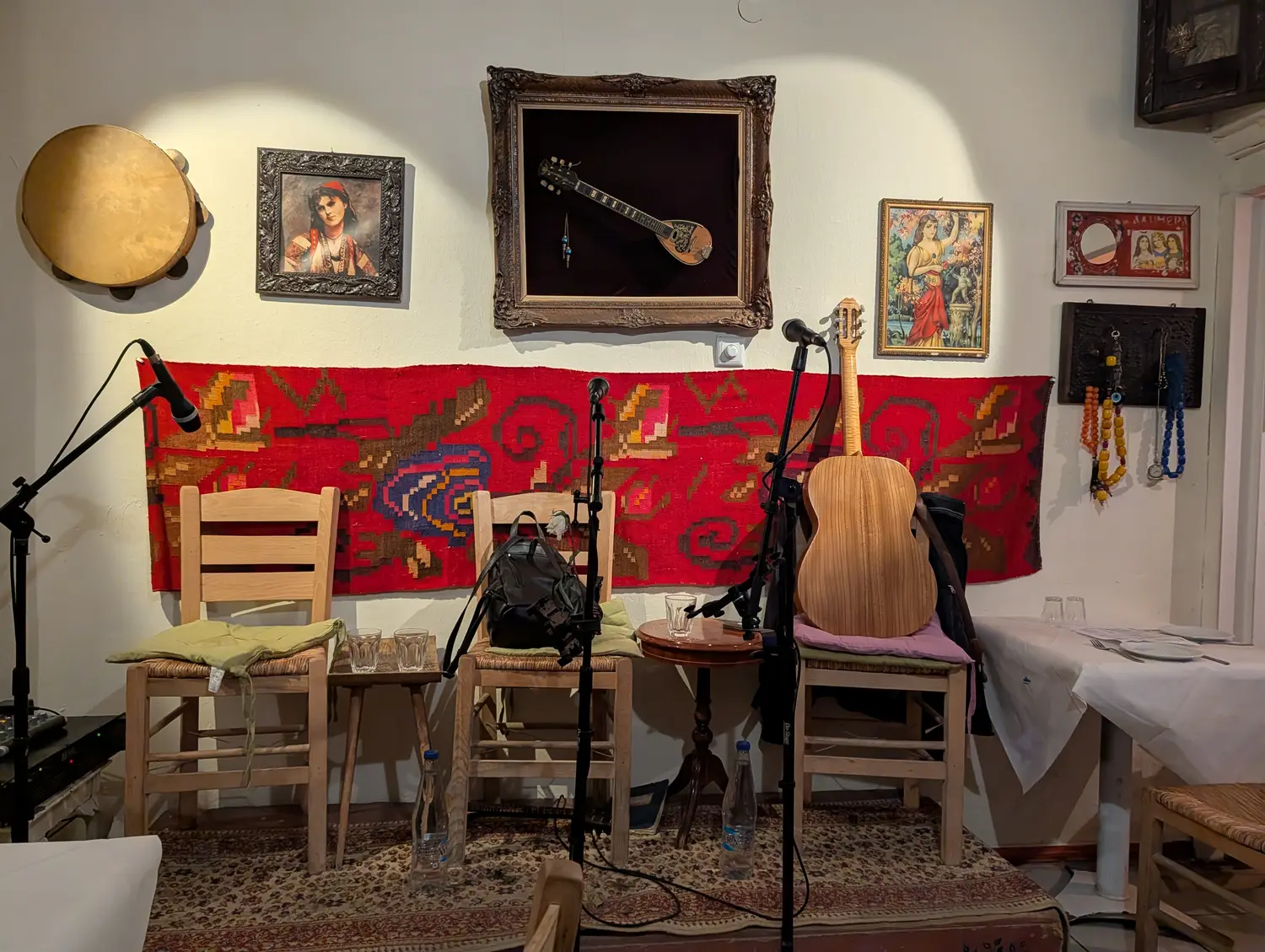 A taverna set up for live music, with a bouzouki and tambourine hung on a whitewashed wall