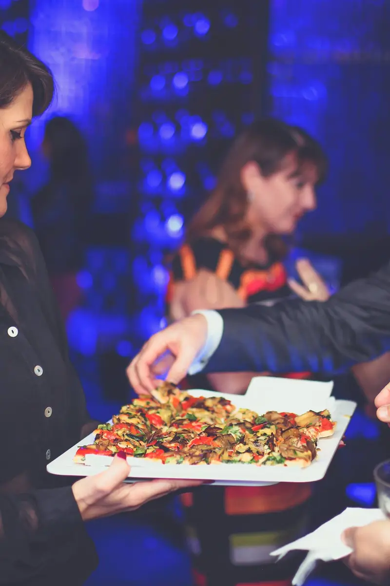 A tray of vegetable canapés being passed among guests under blue lighting