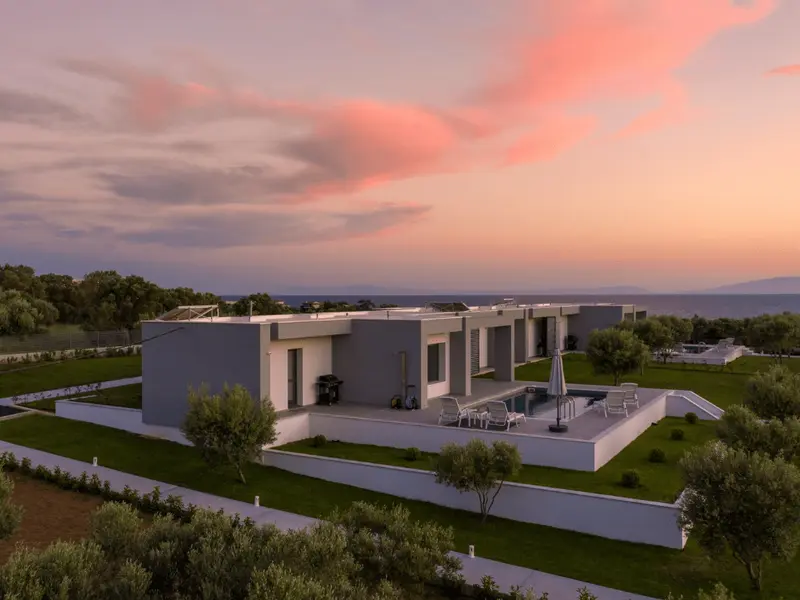 Aerial view as the sky turns pink, the flat-roofed villa on its lawn terraces with the sea flat behind it