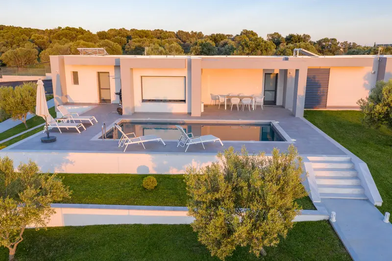 The villa from above in golden light, pool and sun loungers below a run of shuttered rooms