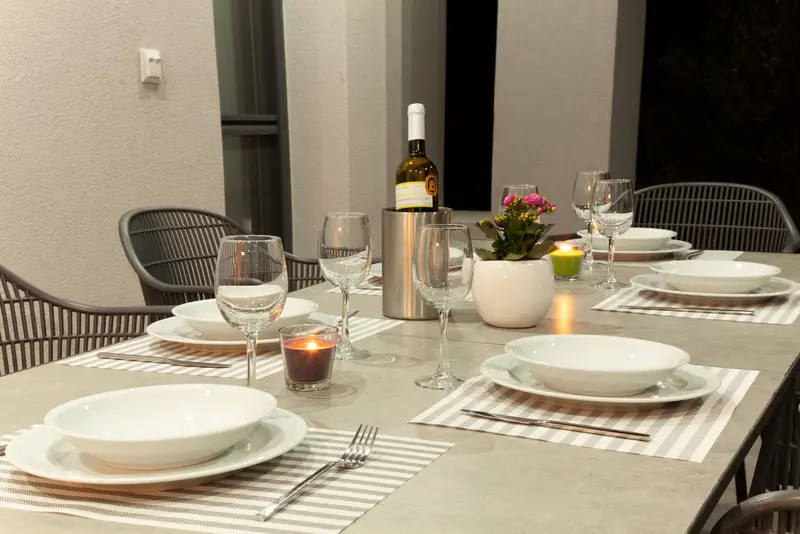 The outdoor table after dark, laid with white bowls, striped mats, candles and a bottle in a cooler