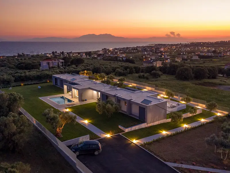 Aerial view at sunset, the villa in its olive grove with the gulf, a far mountain range and the lights of a coastal town beyond