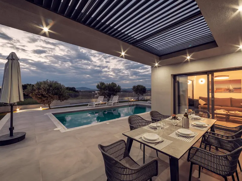 The terrace at blue hour, table set and downlights on, looking across the pool to the loungers