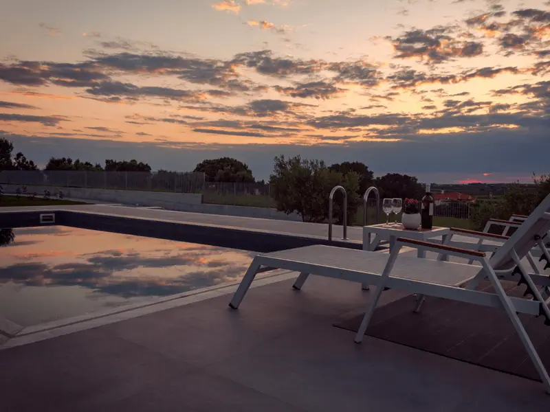 Sun loungers beside the pool at sunset, a bottle of wine and two glasses on the side table, cloud reflected in the water