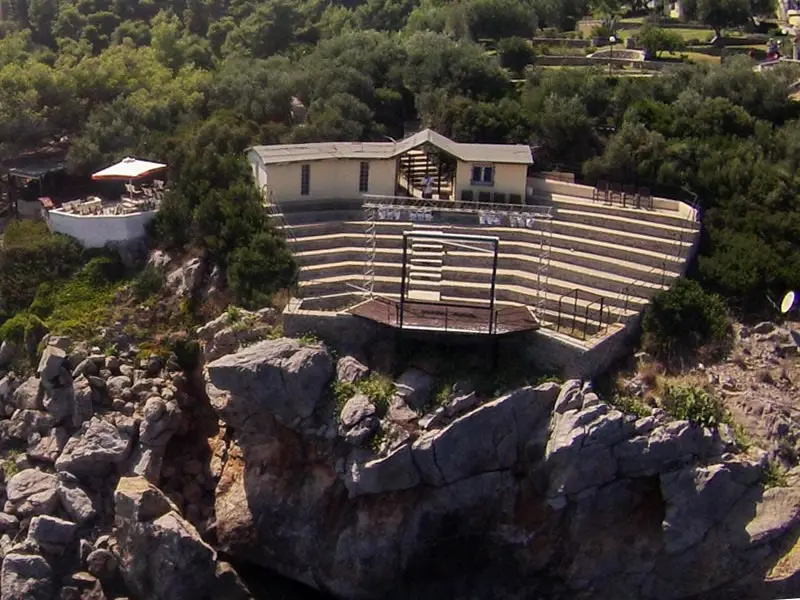 From the air, the stone amphitheatre and its low building on a wooded headland, tiers of seating stepping down to a stage platform at the edge of the rock