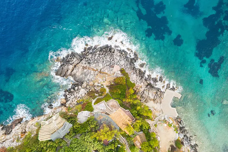 Straight down from above, white water breaking over the rocks below the theatre, its stone steps and the roofs of two small buildings at the bottom of the frame